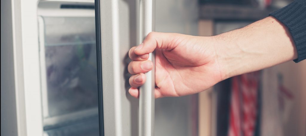 The hand of a young man is opening a freezer door